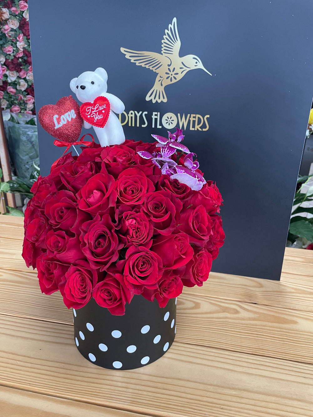 Close-up studio view of the Enchanted Embrace floral design by Days Flowers Florida, capturing the rich velvet texture of dozens of red roses and the elegant details of the accompanying plush toy.