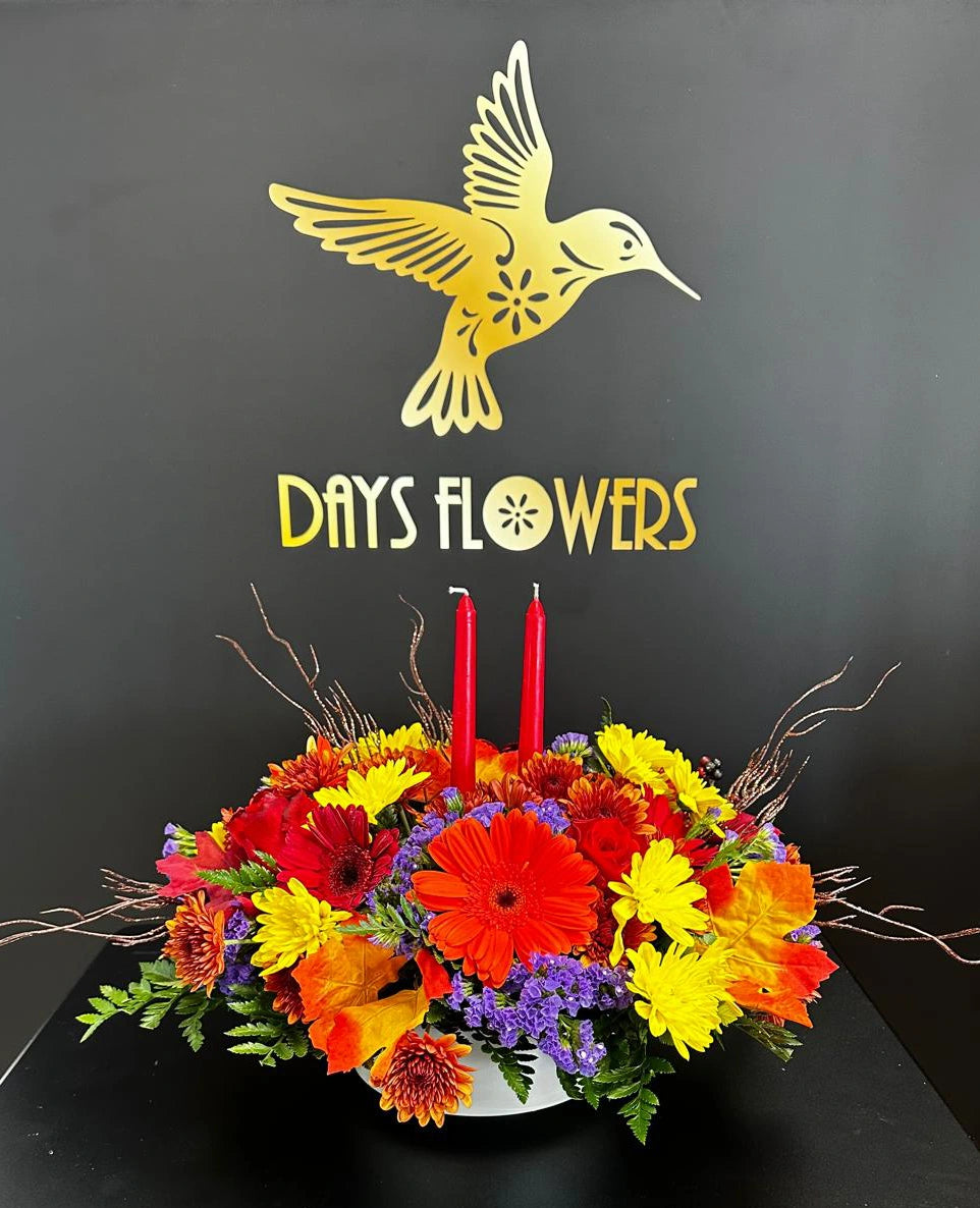 Days Flowers Florida: Thanksgiving centerpiece with red, orange, and yellow flowers and two elegant candles. Warm holiday decor delivery in Summerfield, FL