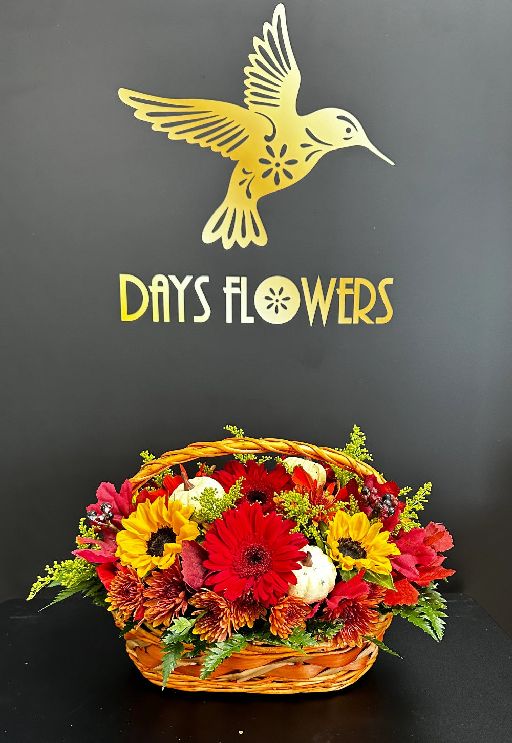 Top-down perspective of the Basket of Gratitude showing a dense mix of sunflowers, red gerberas, and yellow chrysanthemums.