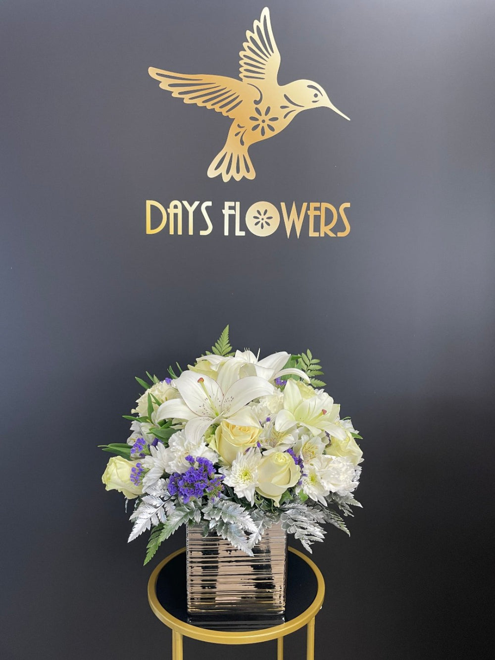 Elegant Serenity Bouquet by Days Flowers Florida featuring premium white roses, baby’s breath, purple statice, silver-dollar eucalyptus, lush greenery, and soft yellow accents in a chic golden openwork vase.