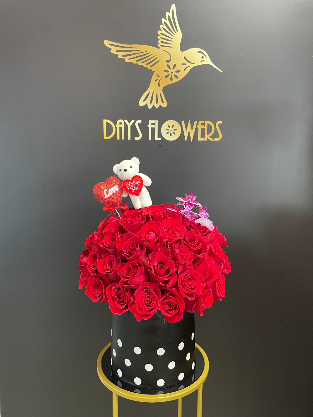A beautiful wide shot of the Enchanted Embrace premium display from Days Flowers Florida, showcasing the massive scale of fifty velvety red roses paired with high-end tropical accents.