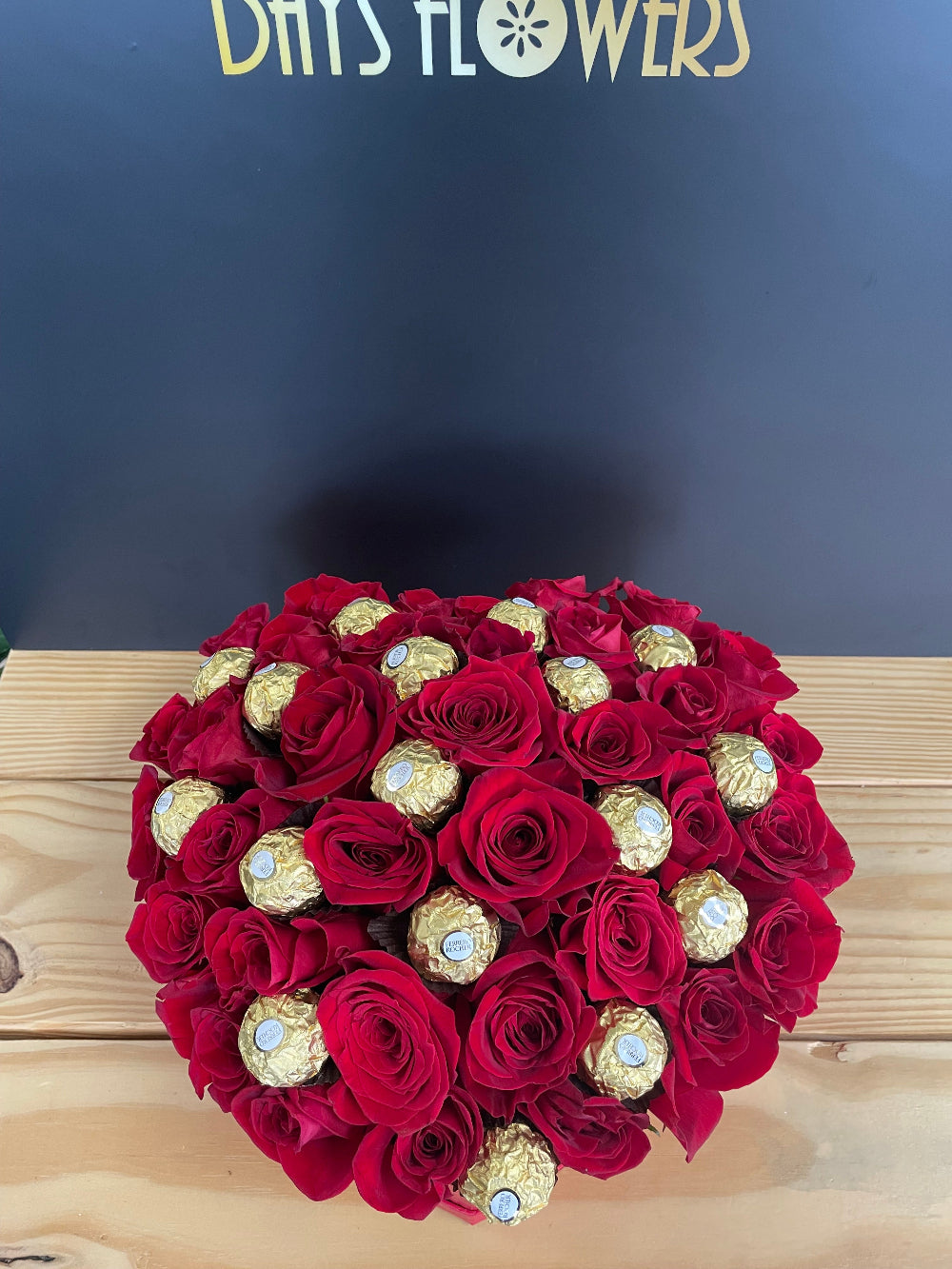 Artistic studio capture of the Romance in a Box designer set, emphasizing the luxury contrasting style that blends crimson roses with iconic golden hazelnut chocolates.