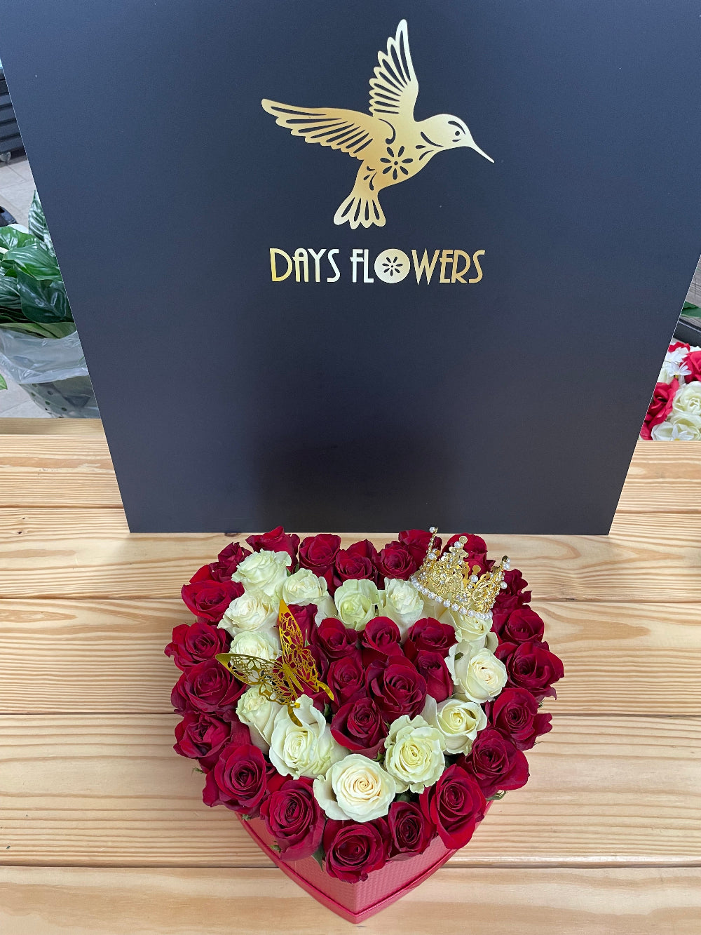 Artistic studio capture of the Royal Bloom Crown floral box, emphasizing the luxury contrasting style that blends crimson and snow-white roses with a decorative golden crown accessory.