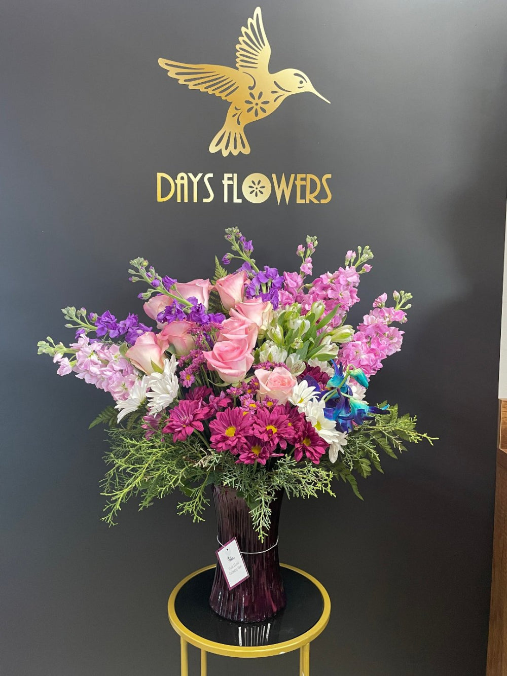 An over two feet tall centerpiece named Steal the Show by Days Flowers Florida, highlighting soaring purple larkspur stems and delicate lavender alstroemeria for a dramatic display.