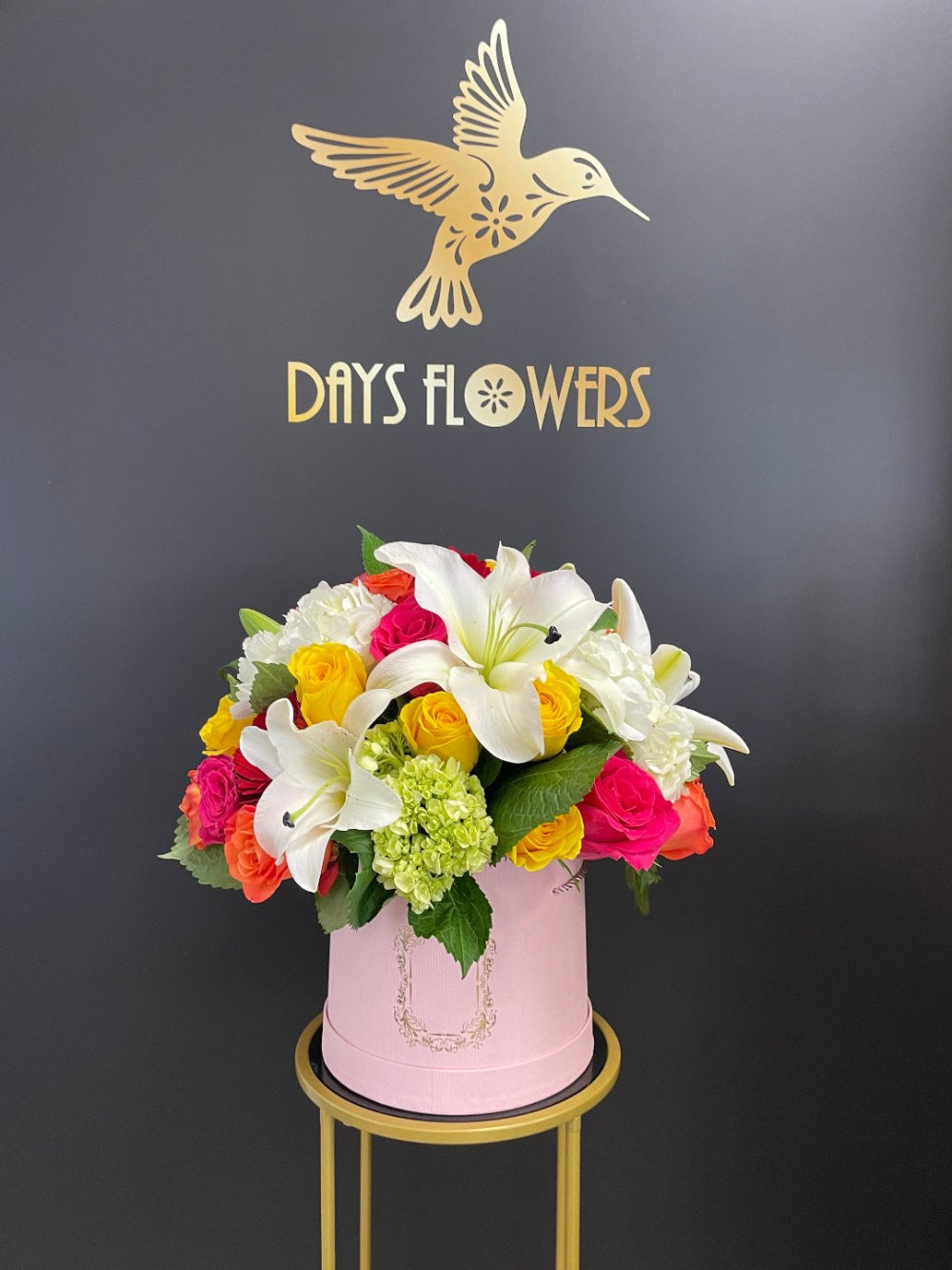 A beautiful close-up of the Sunshine Serenade luxury bouquet from Days Flowers Florida, highlighting vibrant pink and yellow roses contrasted against fresh green hydrangeas in an elegant pink box.