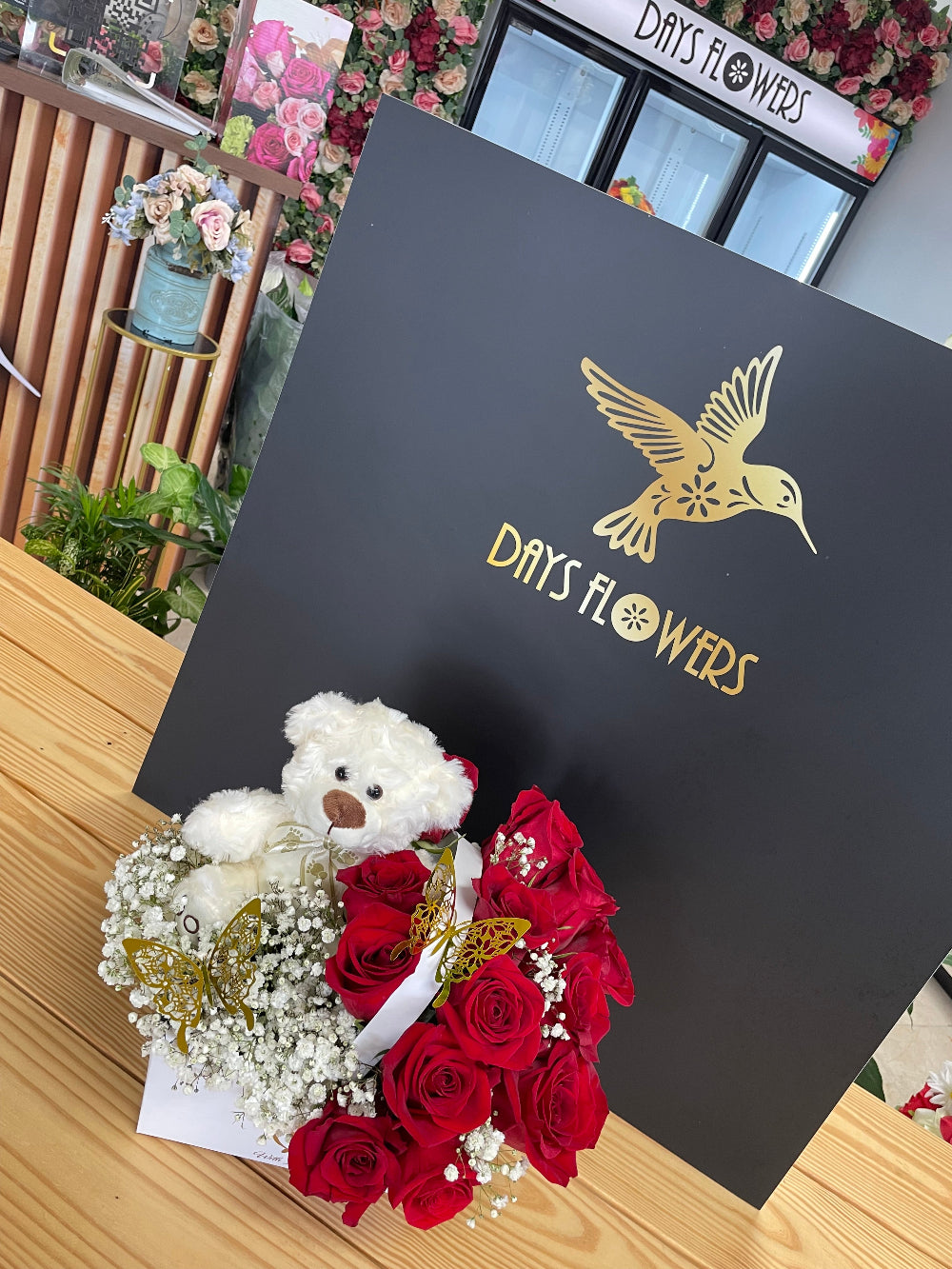 Close-up studio shot of the Teddy Love arrangement by Days Flowers Florida, capturing the playful details of the brown stuffed bear nestled among premium romantic roses.