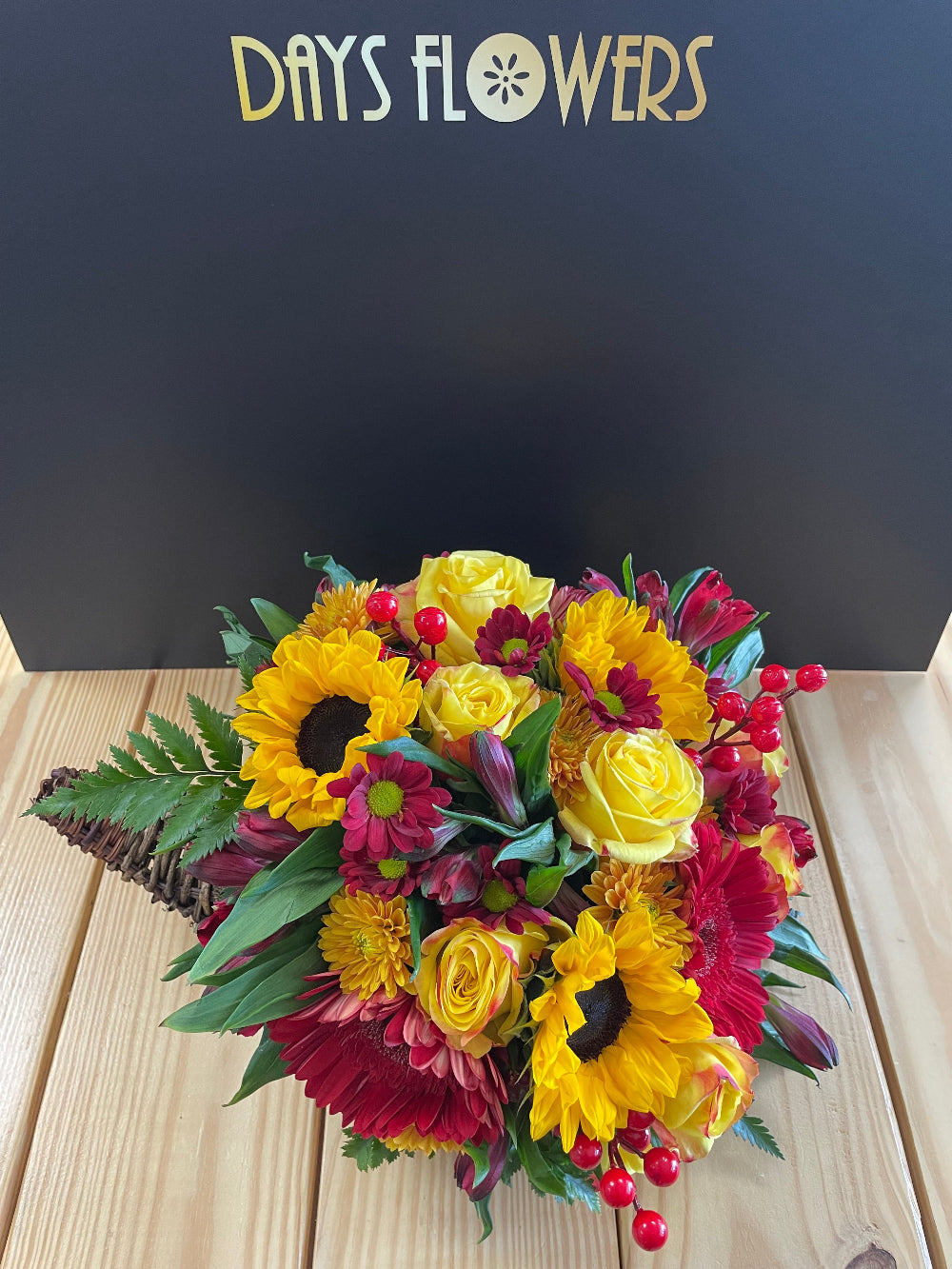 Close-up of the natural wicker cornucopia horn displaying red rose blooms and golden yellow mums