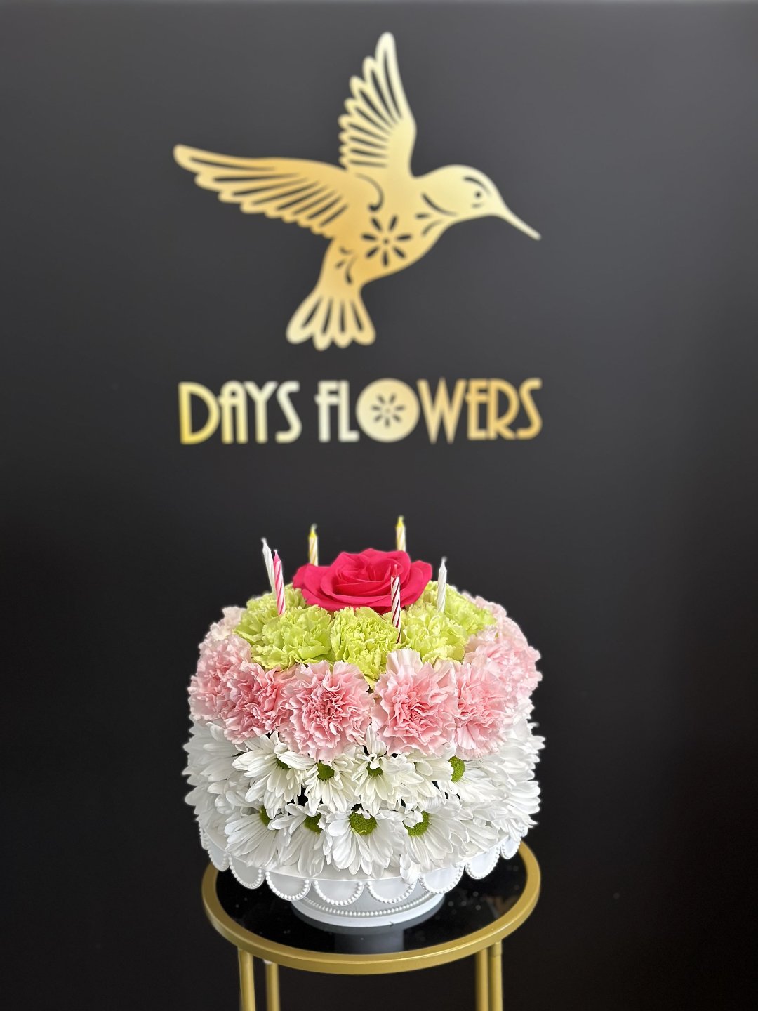 Elegant birthday cake-shaped floral arrangement with pink and white blooms, red roses on a gold stand, perfect gift for delivery in Florida.