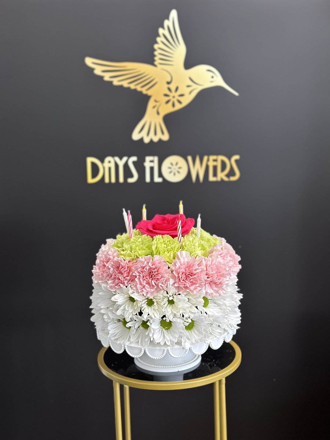 Elegant birthday cake-shaped floral arrangement with pink and white blooms, red roses on a gold stand, perfect gift for delivery in Florida.