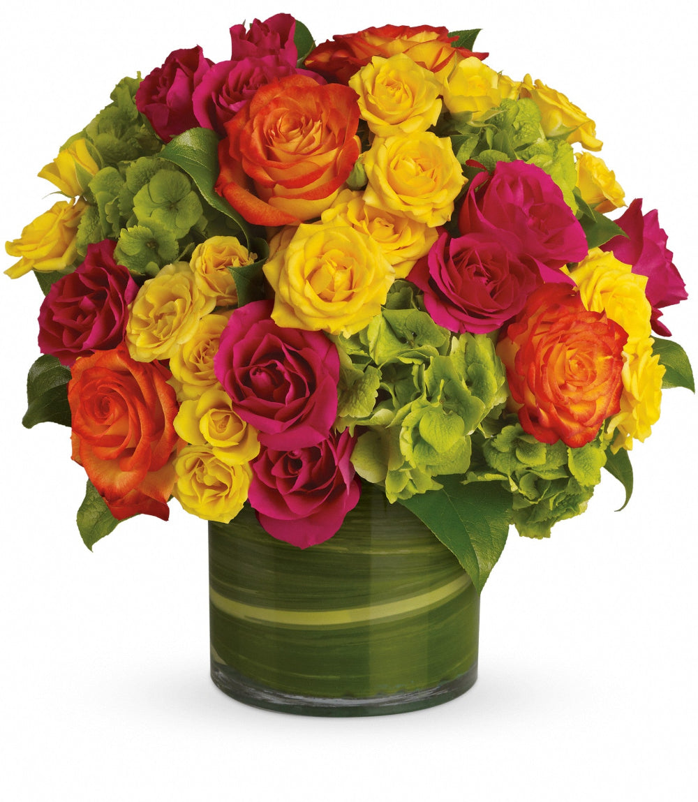 Blossoms in Vogue flower arrangement featuring orange bi-color roses, hot pink spray roses, and green hydrangea in a clear glass cylinder vase by Days Flowers Florida.