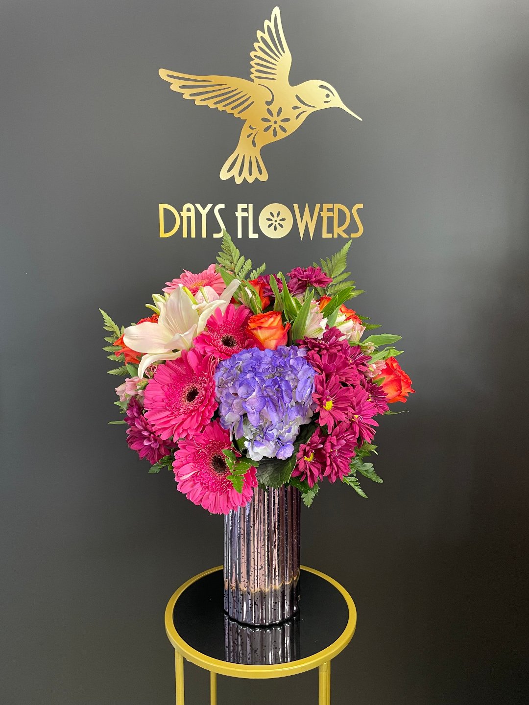 Close-up of the 7.75-inch clear glass couture vase displaying hot pink gerberas and blue hydrangea stems