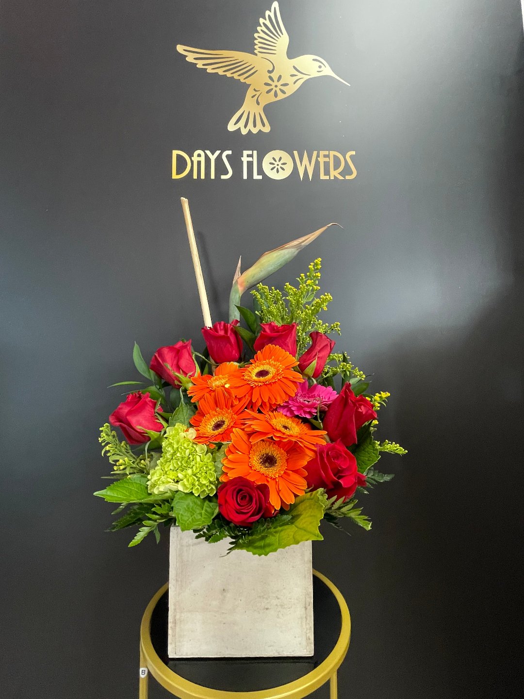 Elegant floral arrangement by Days Flowers featuring vibrant red roses, orange blooms, and lush greenery in a chic white vase, perfect for gifting in Florida areas like Summerfield, Ocala, Orlando, The Villages, and Port St. Lucie.