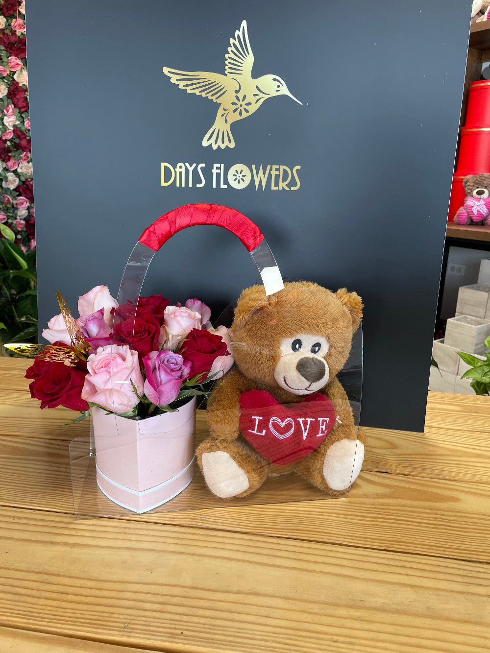 Side perspective of the romantic rose arrangement and teddy bear bundle displayed on a bedroom nightstand