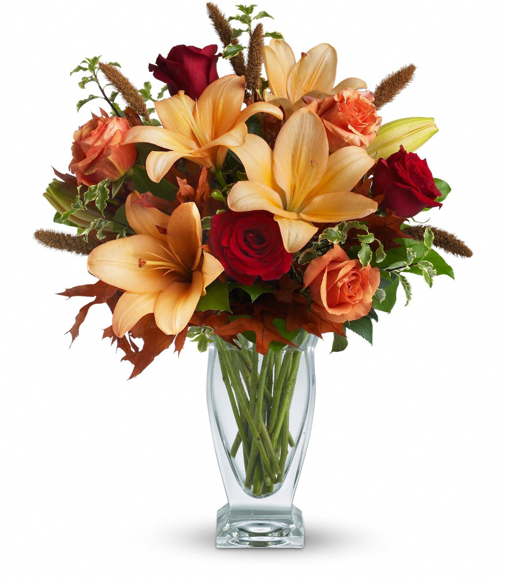 Fall Fantasia bouquet featuring orange roses, red roses, peach asiatic lilies, and dried millet in a clear couture vase by Days Flowers Florida.