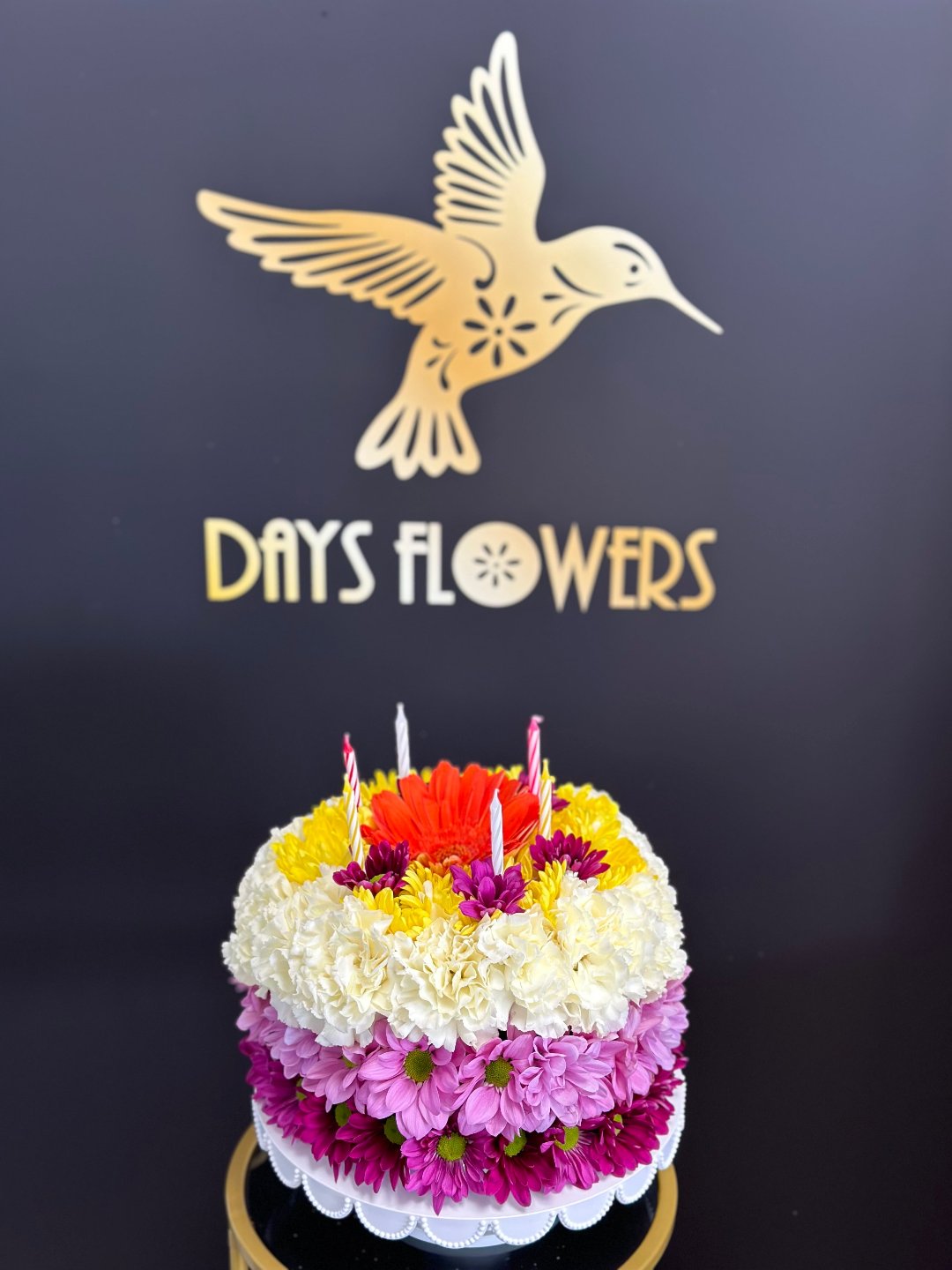 Vibrant floral cake arrangement with purple, white, and red flowers topped with candles, perfect gift from Day’s Flowers in Florida