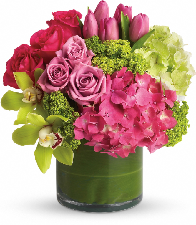 Vibrant bouquet with pink tulips, roses, green hydrangeas, and exotic orchids in a clear glass vase wrapped in a leaf.