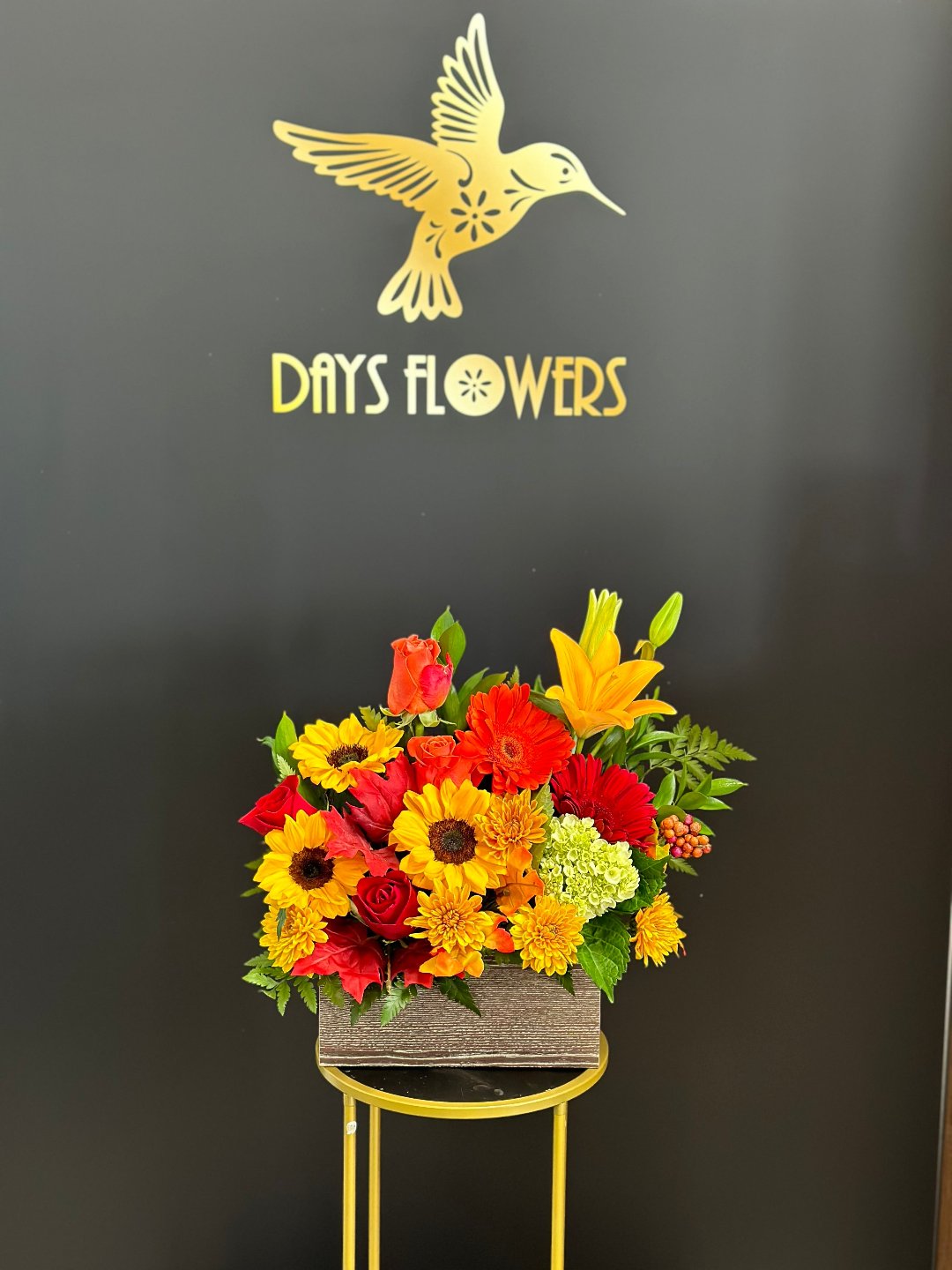 Close-up of the rustic grey wooden planter box displaying fresh red roses and sunny yellow daisy blooms.