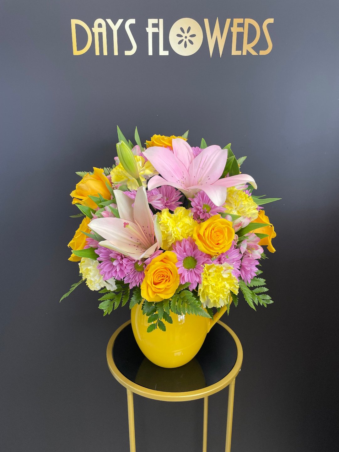 Close-up of the striking yellow vase displaying opening pink lily petals and fresh green leaves