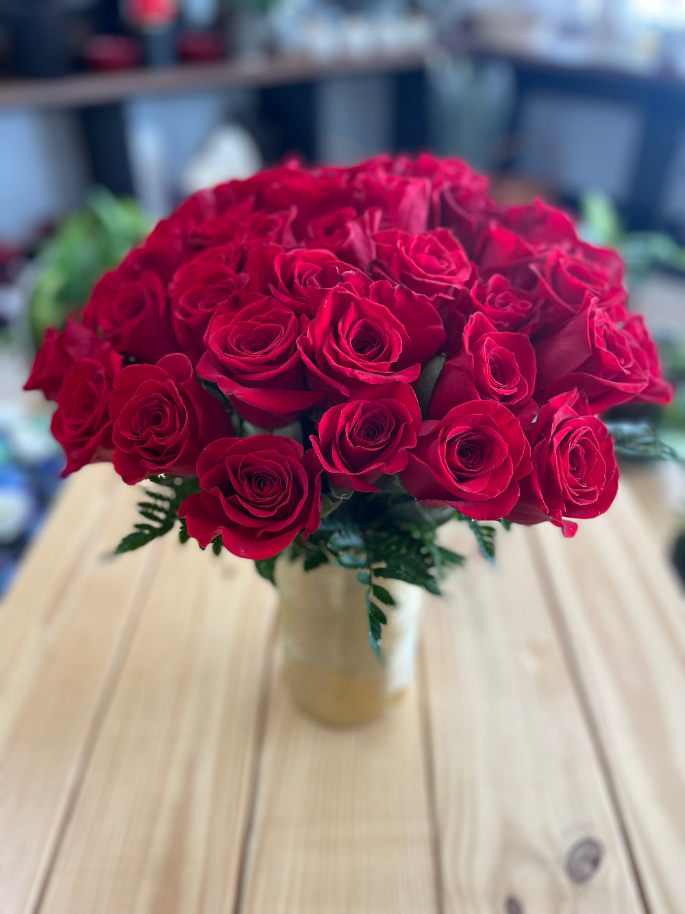 Close-up of the large gold dipped vase displaying thick red rose stems and fresh green salal tips.