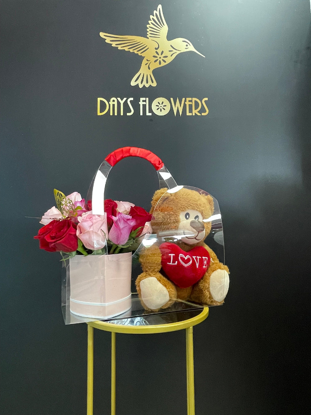 Close-up of the adorable plush teddy bear holding a red LOVE heart beside fresh red rose stems