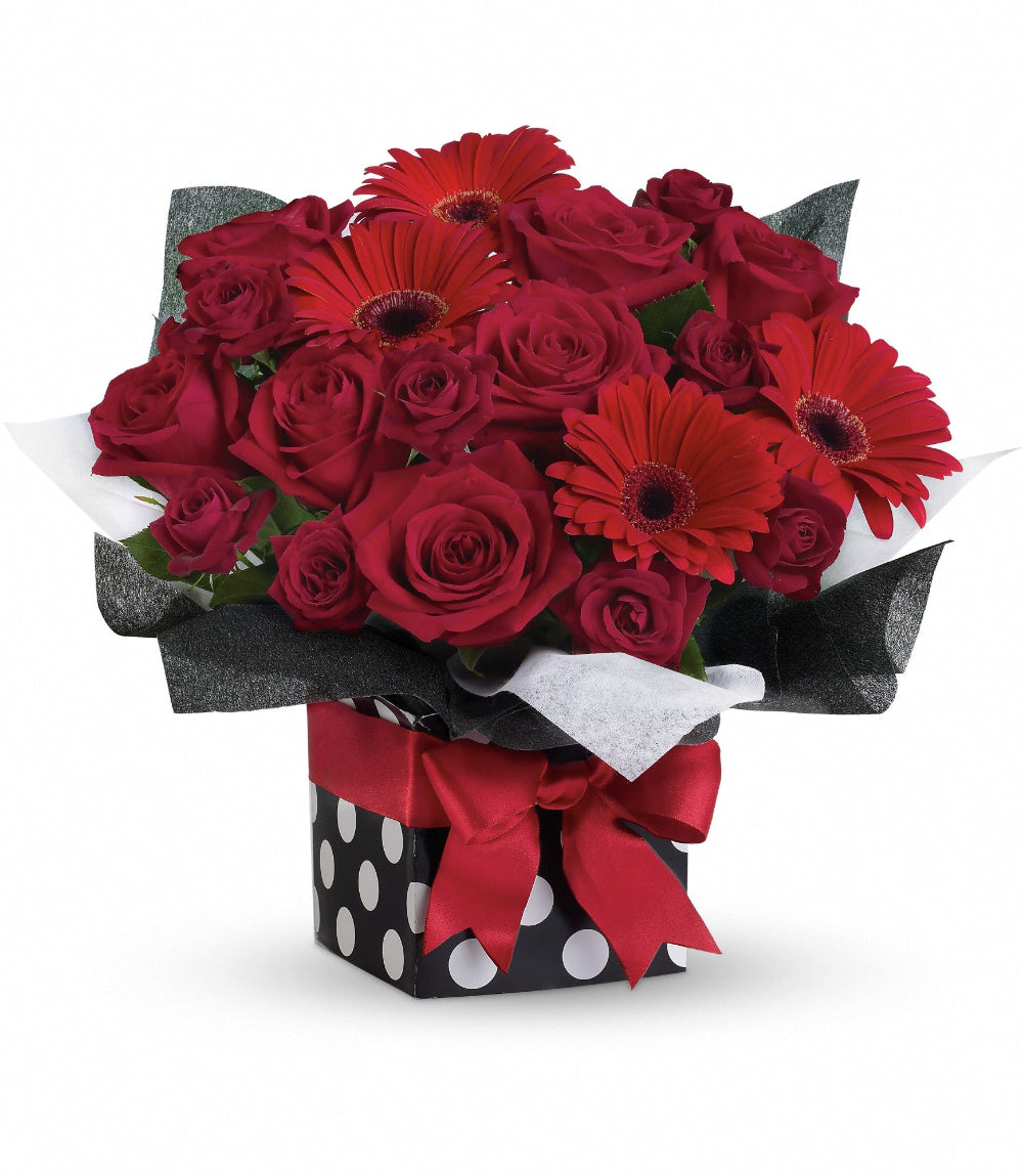 Close-up of the polka-dot present container tied with a brilliant red ribbon displaying red rose blooms