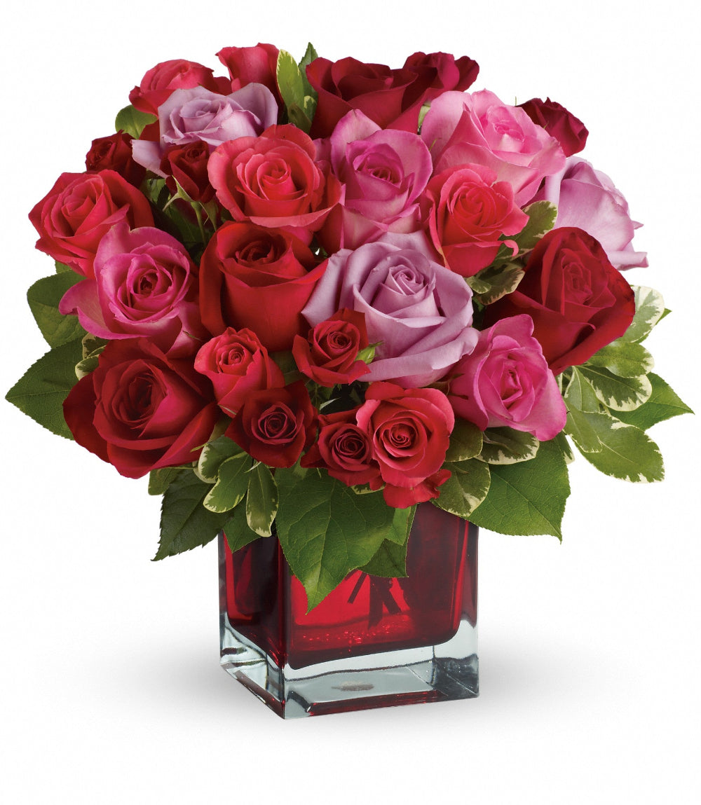 Close-up of the square red glass cube vase displaying opening hot pink, lavender, and red roses