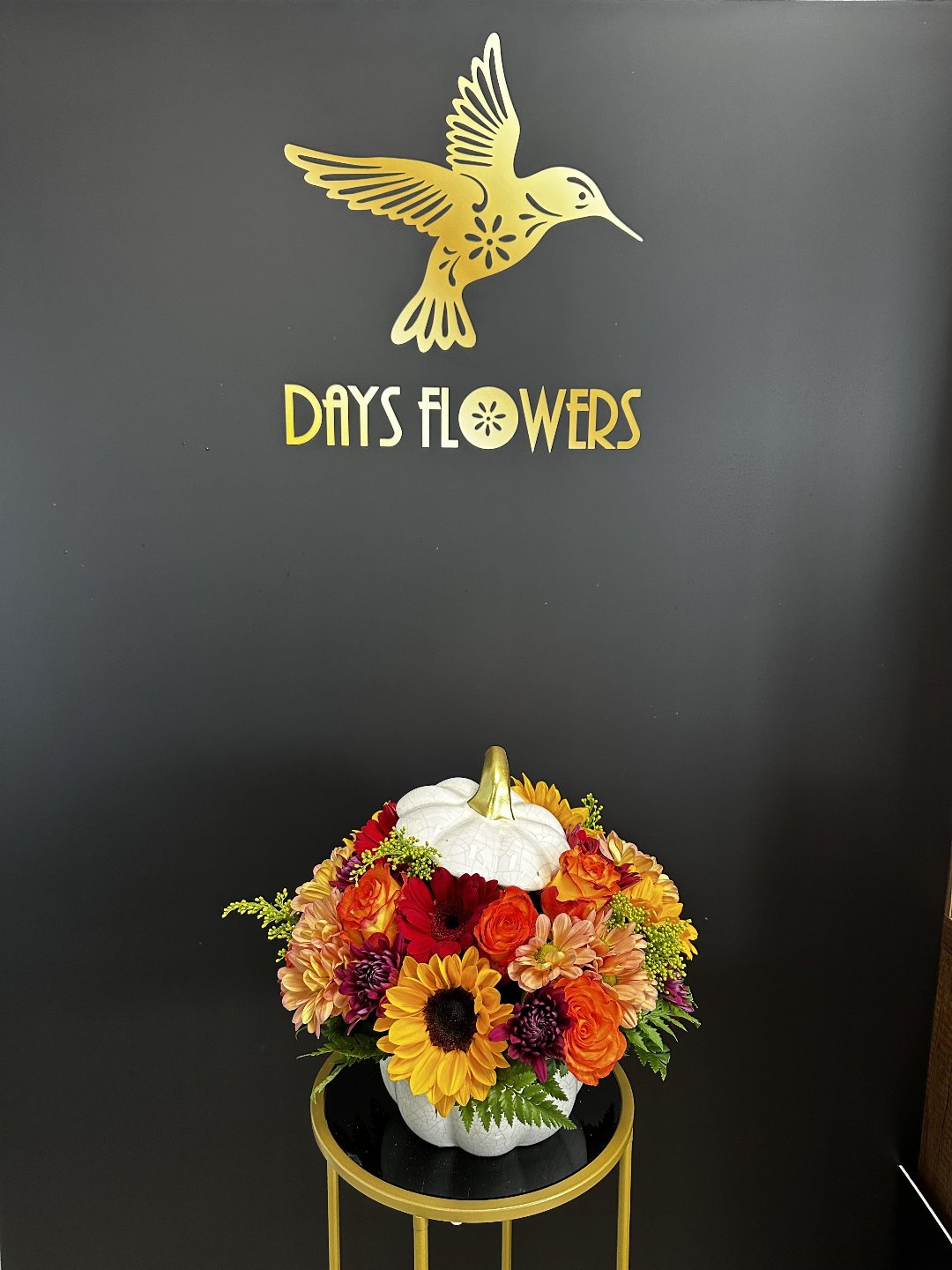Top-down perspective of the Autumn Splendor arrangement showing sunflowers paired with red daisies and orange roses.