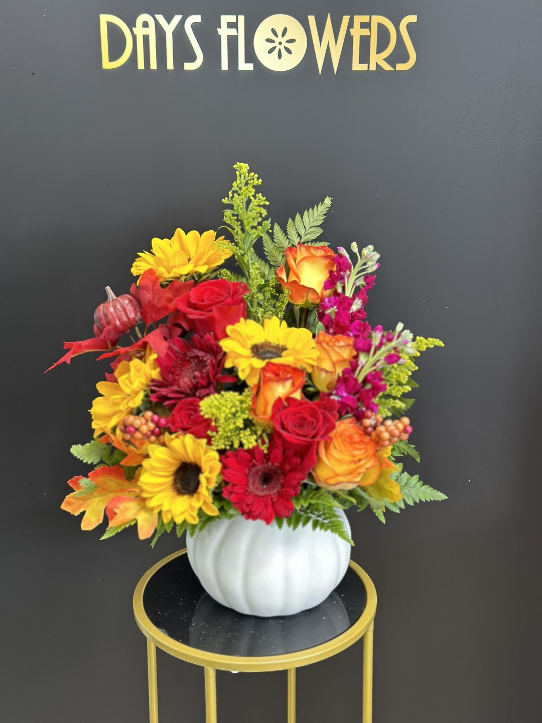 Vibrant bouquet of red, orange, and yellow flowers in a white pumpkin vase, perfect gift from Day’s Flowers in Florida.