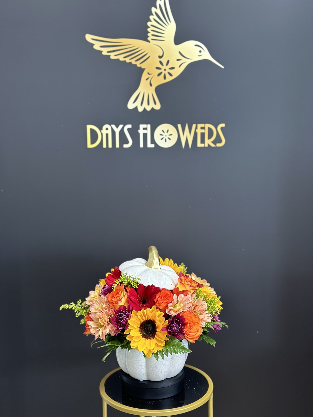 Close-up of the white ceramic pumpkin vase with a metallic gold stem displaying orange rose petals and fall greenery.